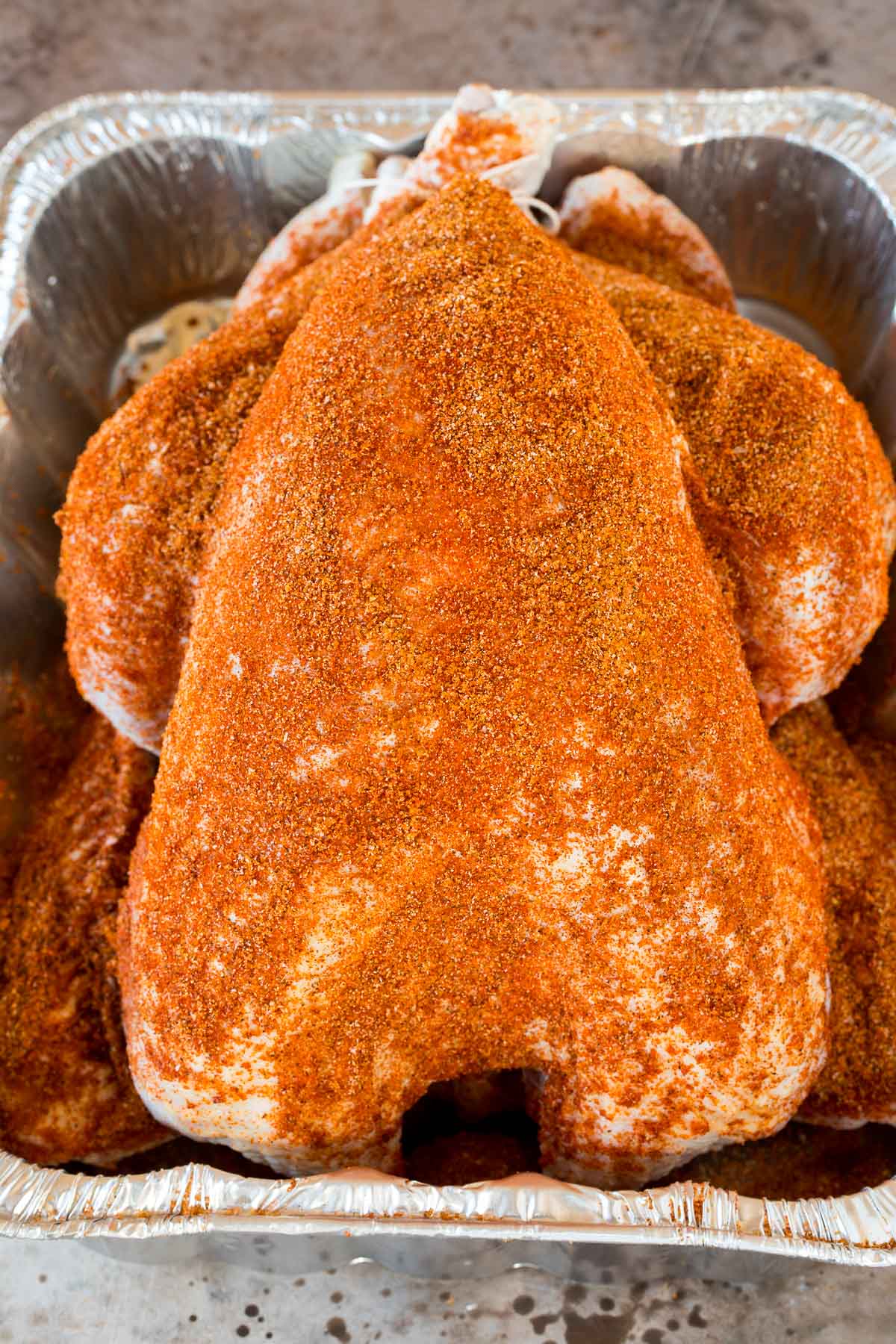 A raw turkey coated in seasoning in a pan.