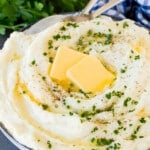 A bowl of sour cream mashed potatoes topped with butter and herbs.