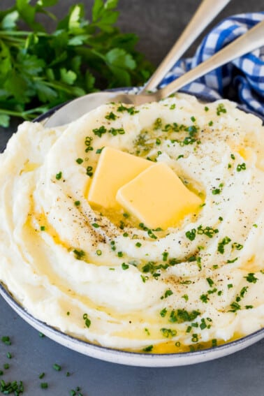 A bowl of sour cream mashed potatoes topped with butter and herbs.