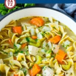 A pot of turkey soup with turkey, noodles and carrots.