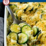 A baking dish with creamy zucchini gratin being served with a metal spoon.