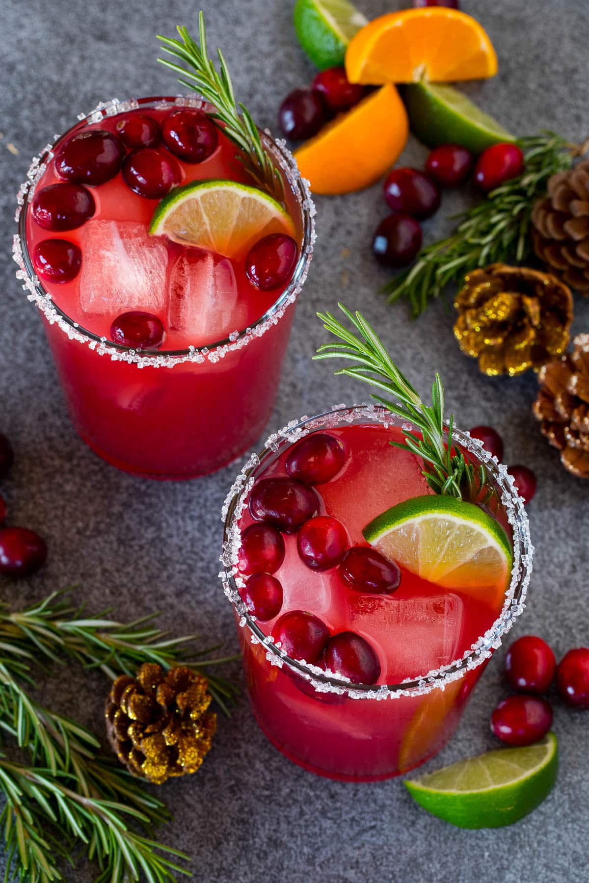 Two glasses of Christmas margarita with sugar rims and garnishes of fresh cranberries and rosemary.