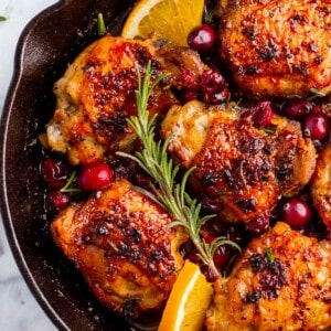 A skillet of cranberry chicken thighs with fresh cranberries, orange and rosemary.