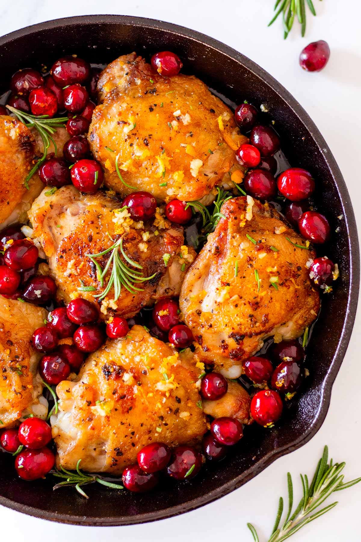 Seared chicken in a pan with cranberries, orange and fresh rosemary.