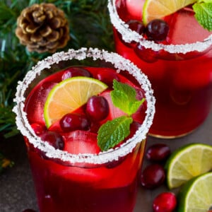 A cranberry margarita in a sugar rimmed glass with garnishes of fresh berries, lime and mint.