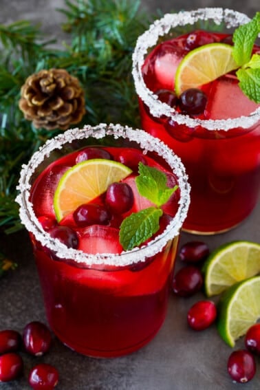 A cranberry margarita in a sugar rimmed glass with garnishes of fresh berries, lime and mint.