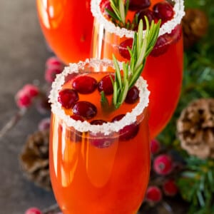 A cranberry mimosa with a sugared glass rim, and a garnish of cranberries and rosemary.