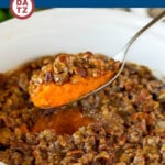 A crock pot sweet potato casserole with a serving spoon lifting some of the casserole.