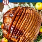 A ham covered in ham glaze on a platter with herbs and fruit.