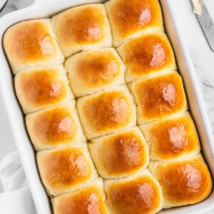 A pan of homemade dinner rolls with butter and a knife on the side.