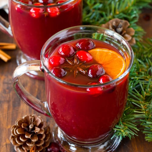 Mugs of Kinderpunsch topped with cranberries and orange slices.