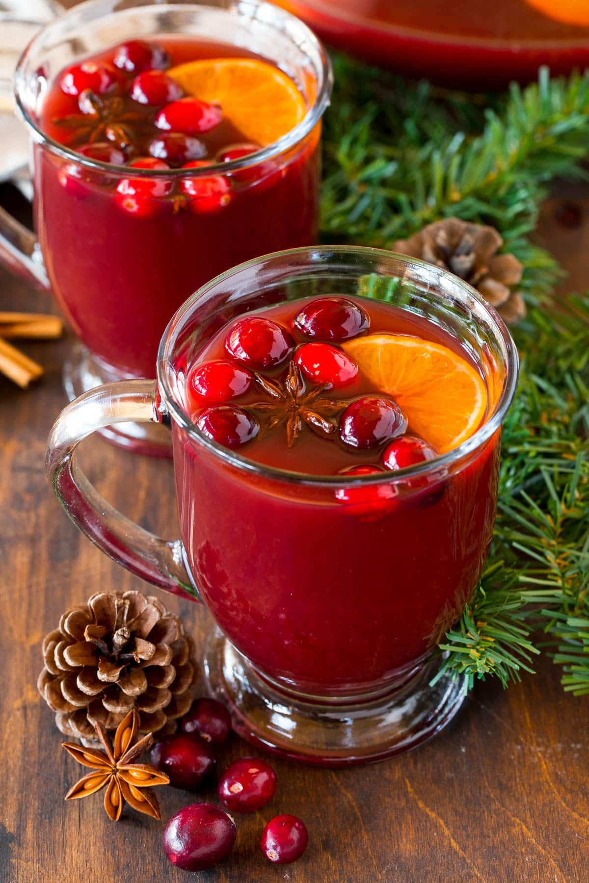 Mugs of Kinderpunsch topped with cranberries and orange slices.