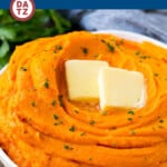 A bowl of mashed sweet potatoes with a pat of butter and garnished with parsley