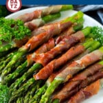 A plate of prosciutto wrapped asparagus piled high and garnished with herbs.