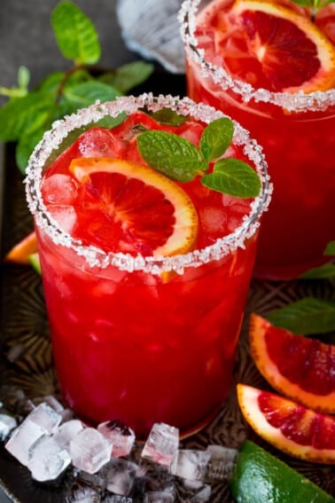 A glass of blood orange margarita with a sugar and salt rim and mint for garnish.