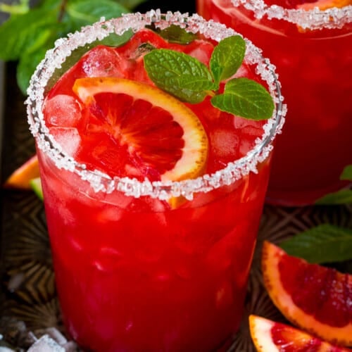 A glass of blood orange margarita with a sugar and salt rim and mint for garnish.
