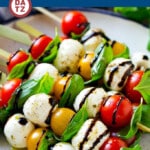 Several caprese skewers stacked on a plate with balsamic glaze on top.