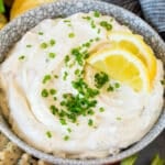 A bowl of clam dip topped with chives and lemon slices.