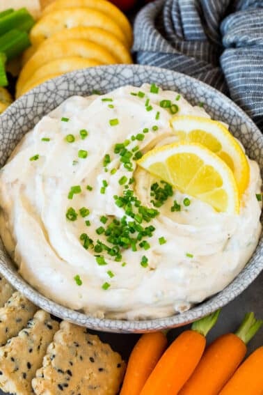 A bowl of clam dip topped with chives and lemon slices.