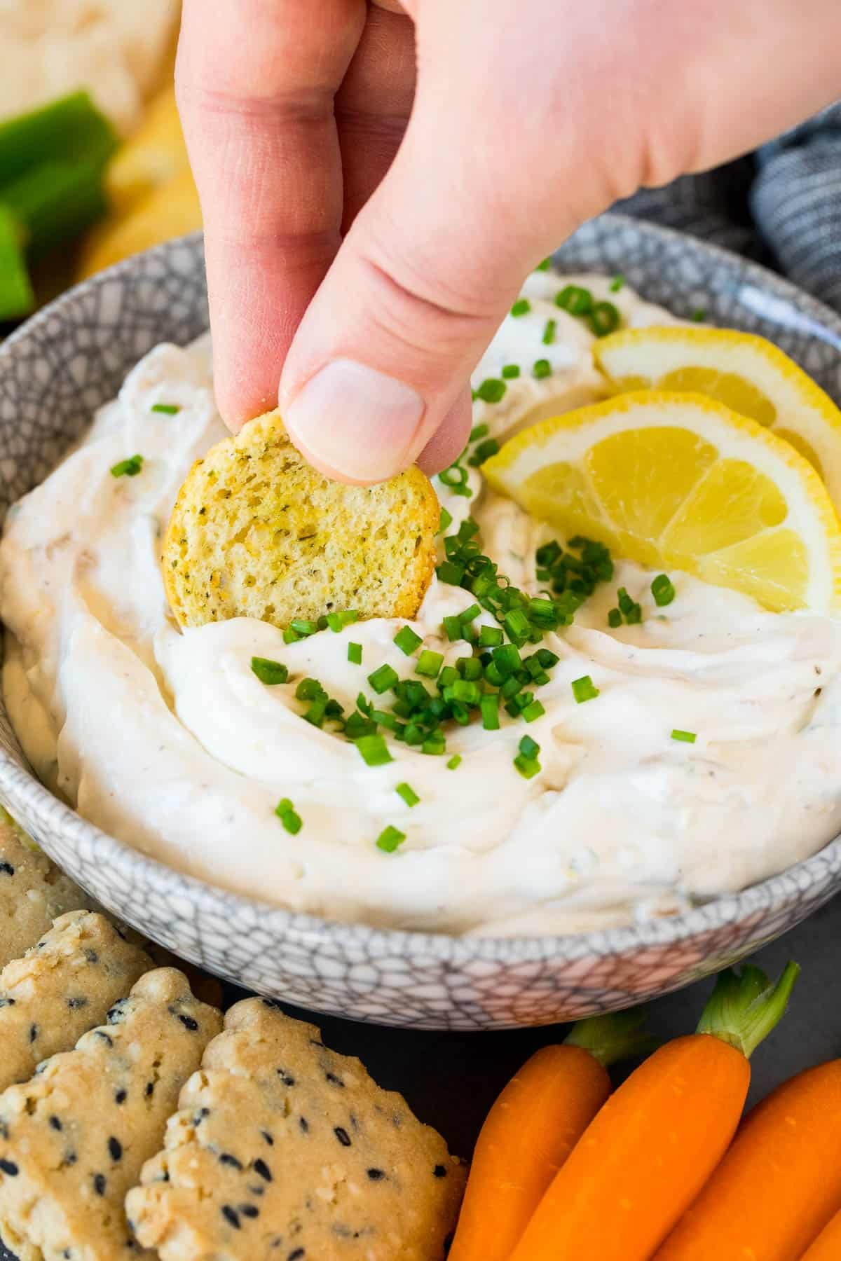 A hand using a cracker to scoop up clam dip.