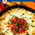 A skillet of hot crab dip with diced tomatoes and sliced green onions on top.