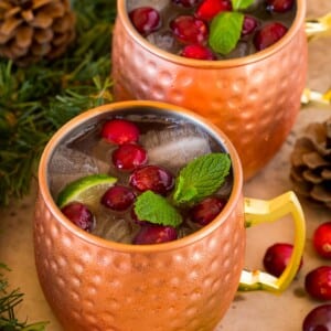 Mugs of cranberry moscow mule topped with fresh cranberries.