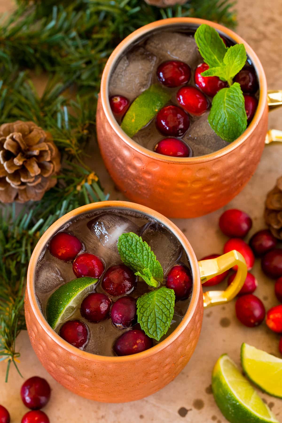 Two copper mugs filled with cranberry moscow mule with fruit and limes for garnish.