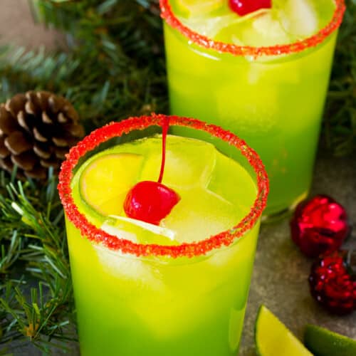 Two cups of Grinch cocktail garnished with cherries and limes.