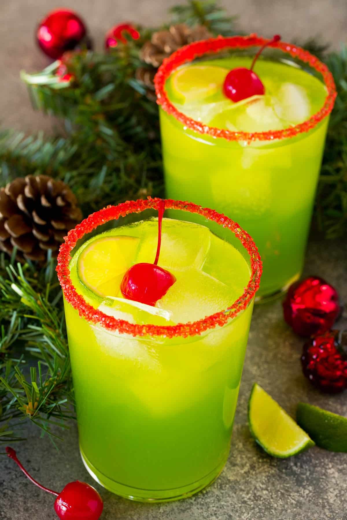 Two cups of Grinch cocktail garnished with cherries and limes.