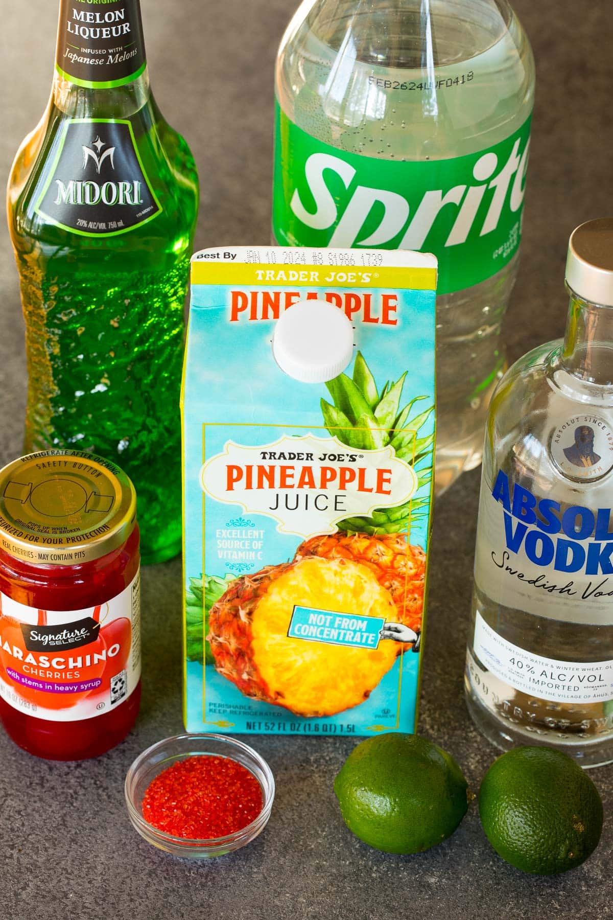 Bottles of juices, liquors, red sanding sugar, cherries and limes.