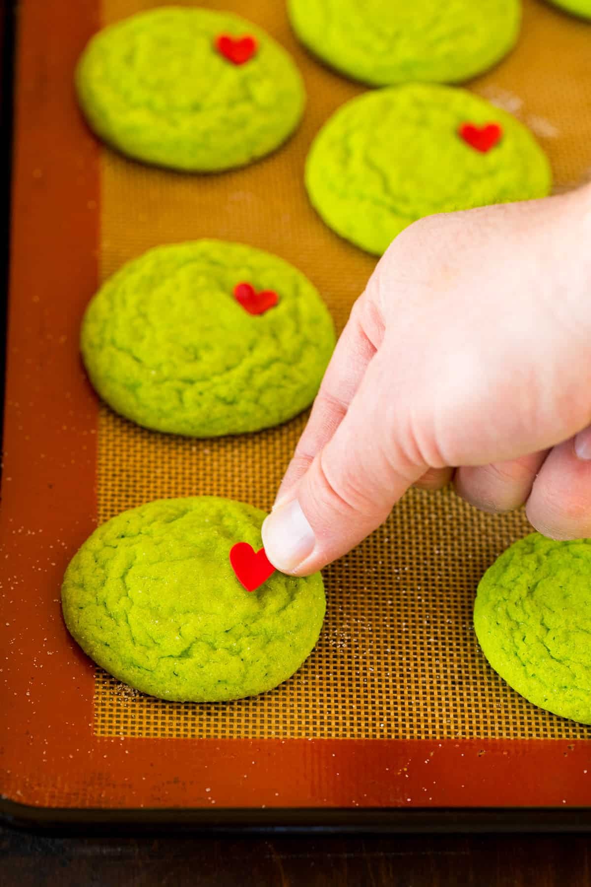 A hand placing a heart sprinkle on top of a cookie.