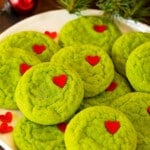 A plate of Grinch cookies with heart sprinkles on top of them.