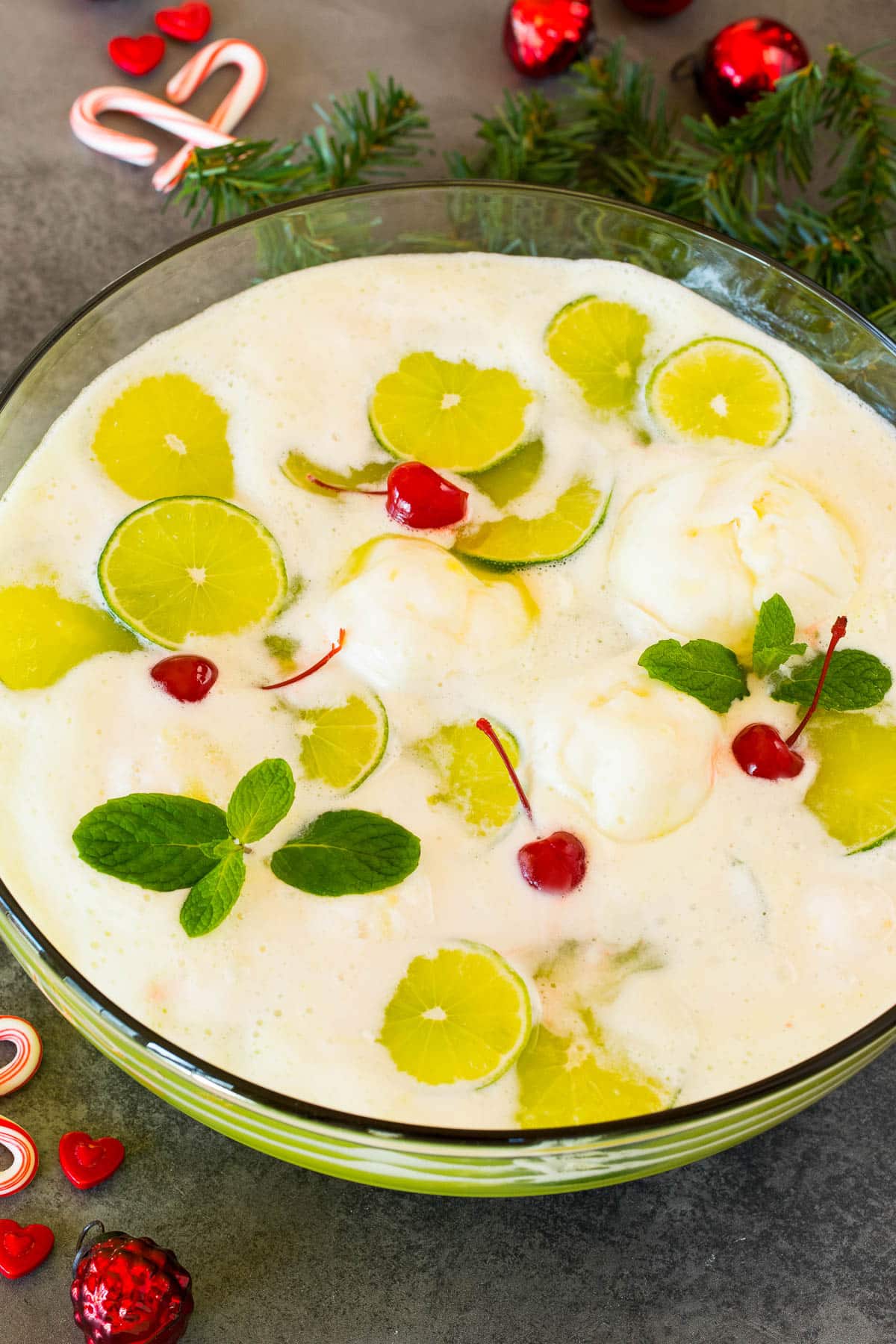 A bowl of Grinch punch topped with cherries, lime slices and mint sprigs.