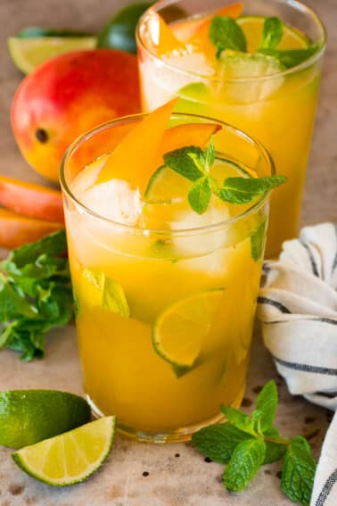 Glasses of mango mojito with garnishes of mint, limes and mango slices.