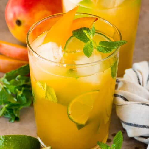 Glasses of mango mojito with garnishes of mint, limes and mango slices.