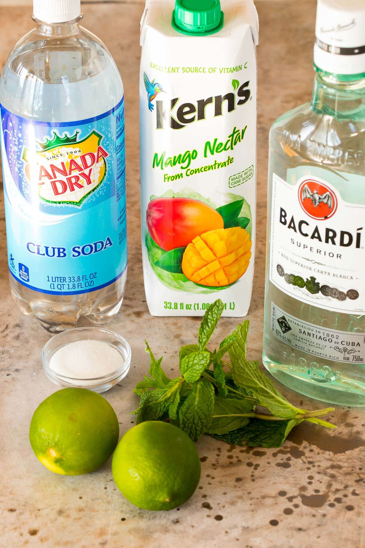 Bottles of rum, mango nectar and club soda with limes, sugar and mint.