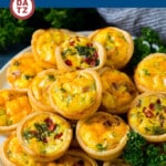 A plate with several mini quiches made with egg, cheese, meat and vegetatbles.
