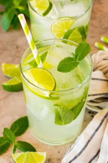 A cup of mojito mocktail garnished with limes and mint, with a green striped straw.