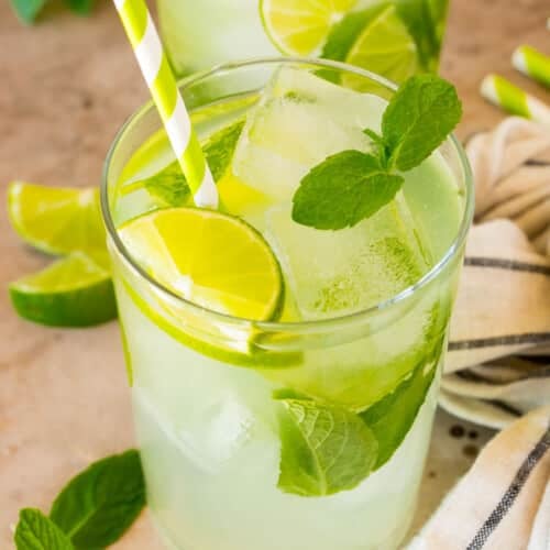 A cup of mojito mocktail garnished with limes and mint, with a green striped straw.