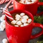 Mugs of peppermint hot chocolate topped with marshmallows and a peppermint stick.