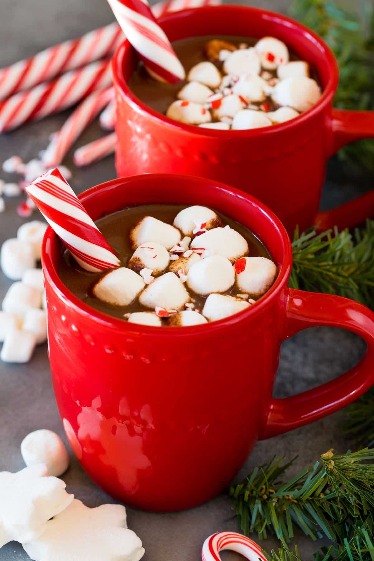 Mugs of peppermint hot chocolate topped with marshmallows and a peppermint stick.