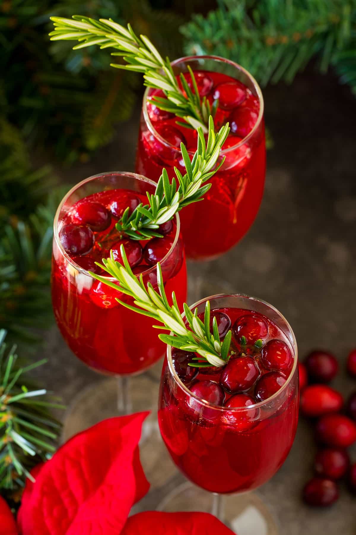 Three glasses of poinsettia cocktail garnished with berries and rosemary.
