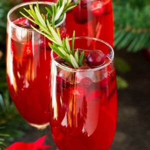 Poinsettia cocktail in champagne flutes garnished with fresh cranberries and rosemary.