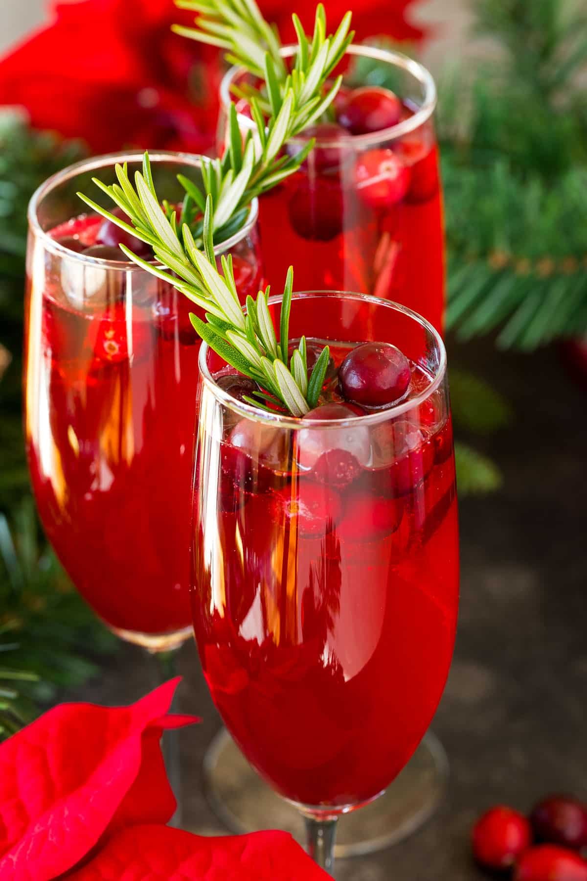 Poinsettia cocktail in champagne flutes garnished with fresh cranberries and rosemary.