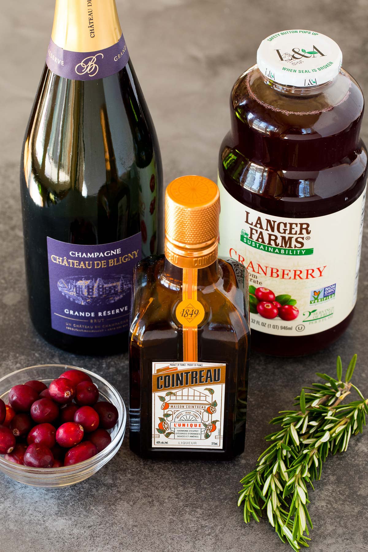 Bottles of champagne, orange liqueur, cranberry juice cocktail, fresh cranberries and rosemary.