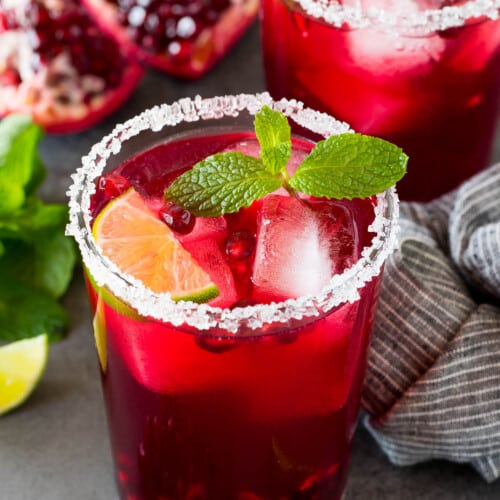A pomegranate margarita in a sugar rimmed glass with mint and lime for garnish.