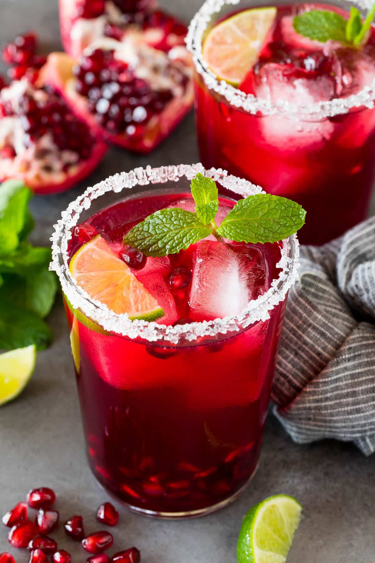 A pomegranate margarita in a sugar rimmed glass with mint and lime for garnish.