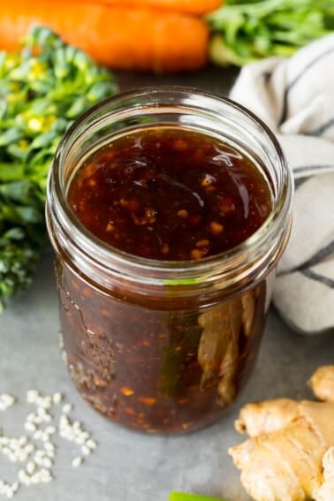 A jar of homemade stir fry sauce surrounded by fresh vegetables.
