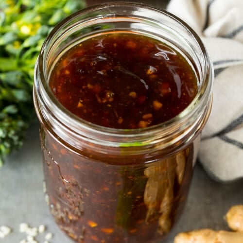 A jar of homemade stir fry sauce surrounded by fresh vegetables.