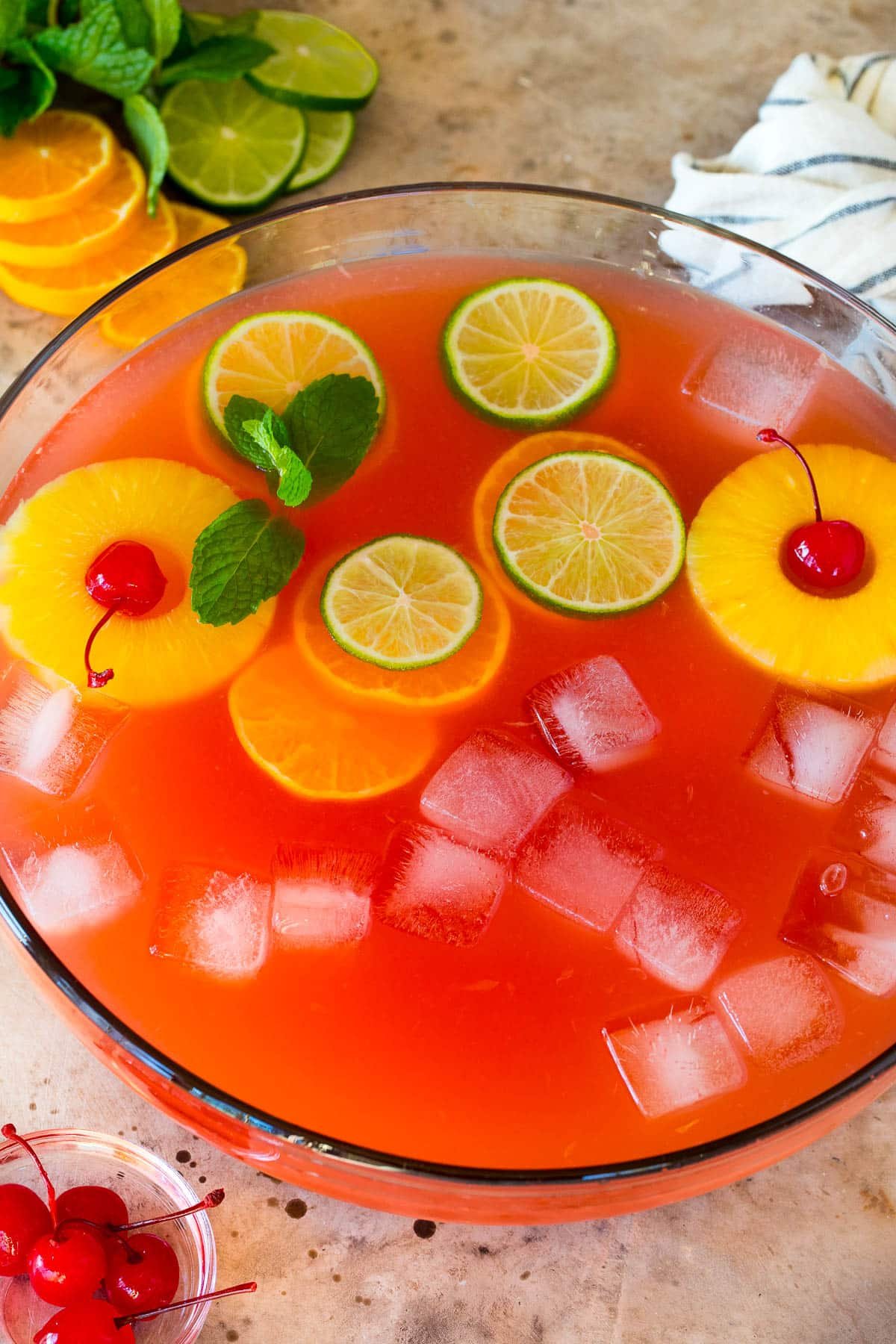 A bowl of vodka punch with citrus slices, pineapple and cherries in it.